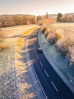 Car driving alone on a winding country road surrounded by frosty landscape, MG4 electric car, deer