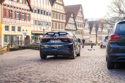 Car drives through a paved street surrounded by historic half-timbered houses, MG4 electric car,