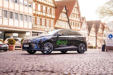 A black car on a cobblestone square surrounded by half-timbered houses in a historic old town, MG4