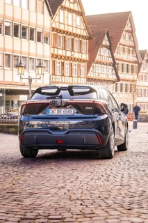 A modern car drives on a cobblestone street in front of half-timbered houses in the old town, MG4