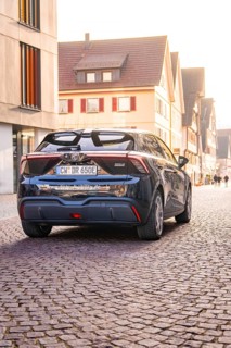 A modern car is parked on a cobblestone street in an old town at sunset, MG4 electric car, deer