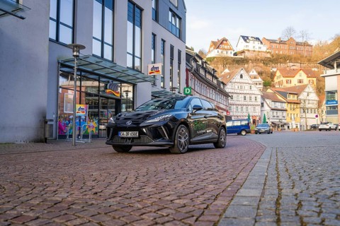Black car in a modern city with paved streets and traditional houses in the background, MG4