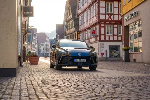 Black car drives through a paved street in a historic city environment with half-timbered houses,