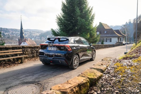 Car driving on a rural road with house and hills in the background, MG4 electric car, Deer