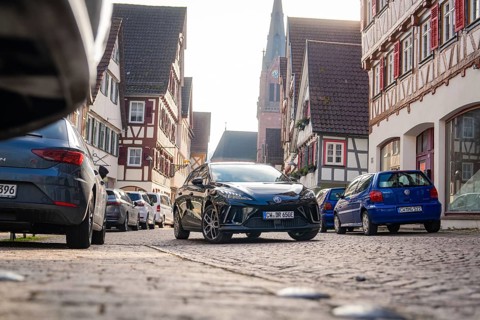 Car in a narrow old town street with half-timbered houses and church in the background, MG4