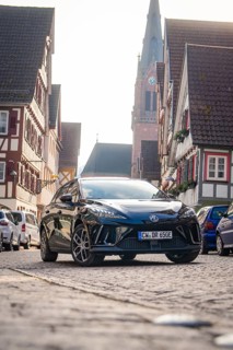 A car in a paved old town street with church and half-timbered houses, MG4 electric car, Deer
