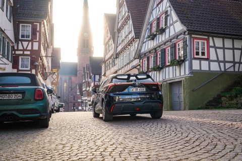 Timbered road with parked cars and church tower in the background in daylight, MG4 electric car,