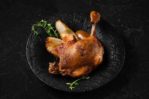 Duck confit on a black stone plate with pieces of roasted pear and herbs. The setting shows a dark