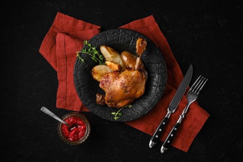 Top view of cooked duck confit on a black stone plate with caramelised pears and lingonberry sauce