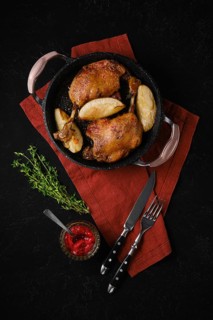 Duck confit with roasted pear in a black skillet served with a bowl of lingonberry jam. Fresh thyme