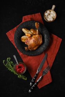 A plate holds a portion of duck confit alongside roasted pears. A small bowl of lingonberry sauce