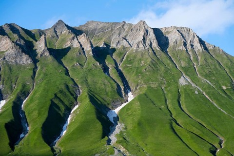 Steep green mountain ridges rise up under a blue sky, mountainous landscape between Gudauri and the