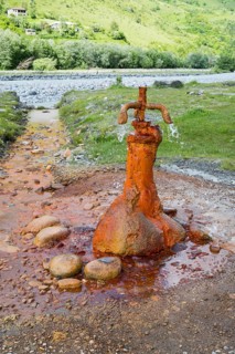 A rusty water spring over stones in front of a green landscape, mineral spring near Nadibani, White