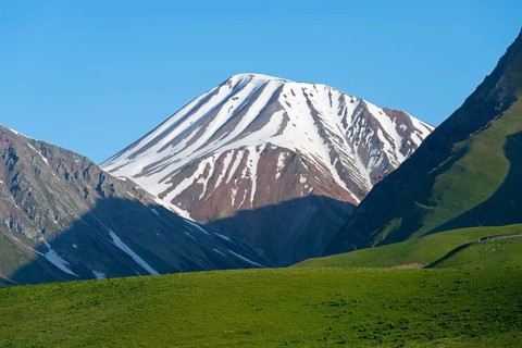 Snowy mountain with shadows cast over green hills, landscape between Kvesheti and Gudauri,