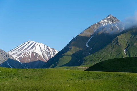 Snow-capped mountains with clouds at the summit, surrounded by green hills, landscape between