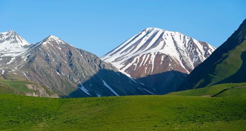 Majestic snow-capped mountains with green fields in the foreground, landscape between Kvesheti and