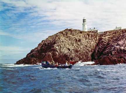 Tour boat passing rocky cliffs at Round Island lighthouse, Isles of Scilly, Cornwall, England, UK