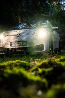 Car in the dark forest, switched on headlights illuminate the mossy ground, VW ID3 electric car,