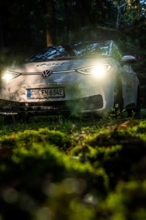 Car with headlights switched on in dark forest on mossy ground, VW ID3 electric car, Deer