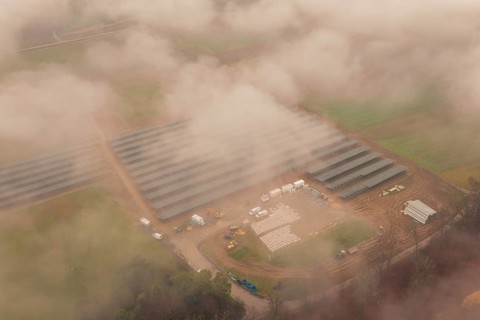 Fog-covered construction site with solar systems, several vehicles visible, energy revolution,