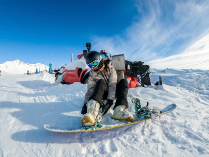 Young woman strapping her snowboard boots into the bindings on a snowy slope under a clear blue