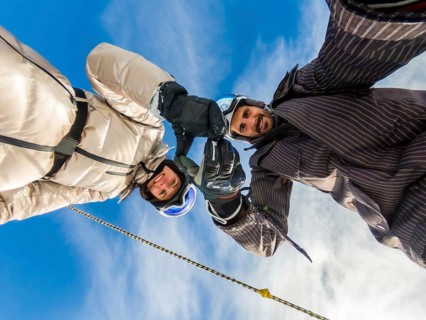 Happy couple wearing skiing gear and helmets, extending their hands upwards, forming an arch