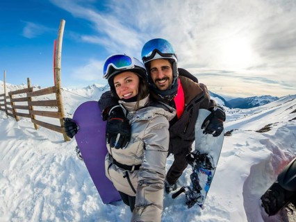 Couple smiling into camera while posing with snowboards on sunny snowy mountain slope, joyful