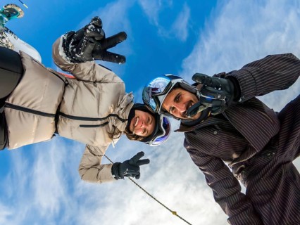 Young couple smiling. Wearing ski helmets and goggles. Making peace signs and thumbs up gestures