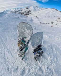 Snowboards rest in deep snow on a high mountain summit, offering a panoramic view of an expansive