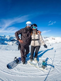 Snowboarders on a sunny mountain peak, smiling couple in helmets and goggles enjoying winter