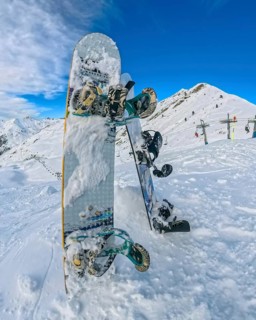 Snowboards planted upright in deep powder at a high altitude ski resort, framed by snow covered