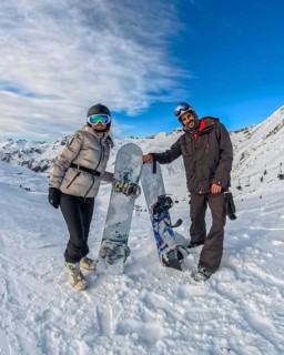Couple standing with snowboards on a snowy mountain slope, smiling under a blue sky while enjoying