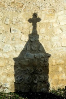 Mazerier village. A shadow of a stone cross appears on an old, weathered stone wall. Sunlight