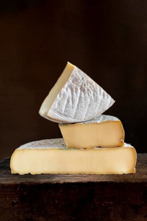 Three pieces of Saint-Nectaire cheese are stacked on top of each other, set on a dark wooden