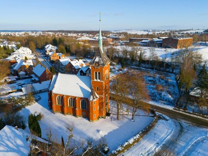 Snowy church with high tower surrounded by snow-covered trees and buildings, aerial view, Trinity
