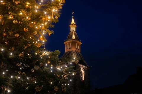 Glowing church tower next to a festively decorated Christmas tree at night, Nagold, Calw district,