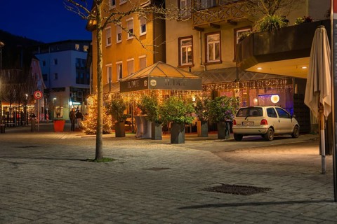 Restaurant with illuminated terrace at night, surrounded by plants and a parked car, Nagold, Calw