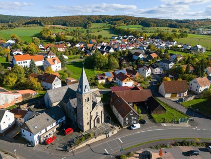 A village with church surrounded by hills and green meadows in autumn, aerial view, Niederkalbach,