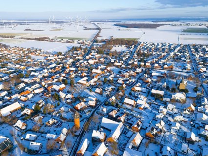 Aerial view of a snowy village with wind turbines on the horizon and a water tower in the center,