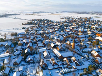 Bird's-eye view of village, with snow-covered roofs, a water tower and vast, snow-covered fields,