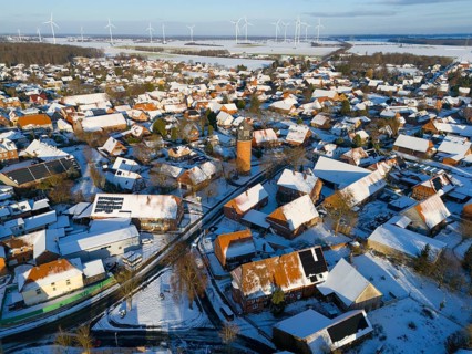 Snowy village with a water tower and a variety of wind turbines in the distance under a clear sky,