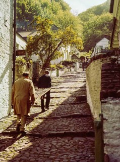 Men carrying wooden sled or sledge used for transport on steep hill of cobbled main village street,