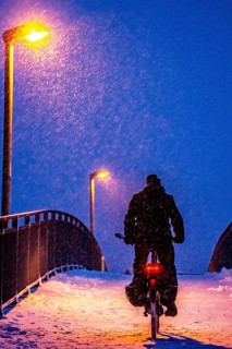 Winter weather, blowing snow, person with e-bike, bicycle on snowy bridge, footpath bridge, steep