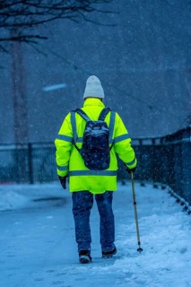 Winter weather, blowing snow, man walking on a snowy sidewalk with a walking stick, North