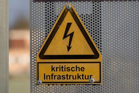 (Photo montage) Text CRITICAL INFRASTRUCTURE on a warning sign for a high-voltage line