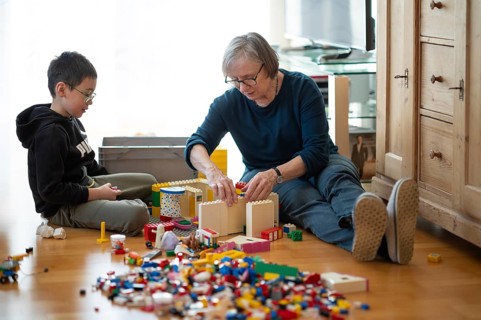 Elderly woman, grandma, boy, 6 years, grandson, glasses, multi-ethnic, playing together with Lego,