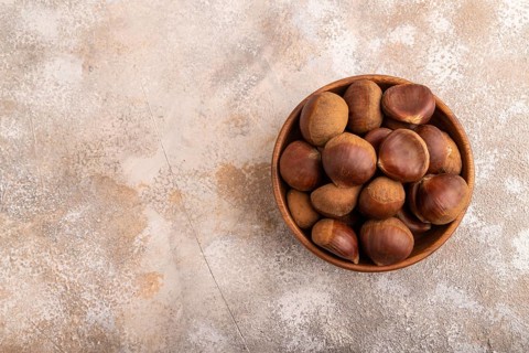 Wooden bowl with raw edible ?hestnuts on brown concrete background, top view, flat lay, copy space,