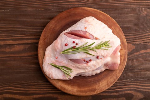 Raw Turkey Thigh with spices and rosemary on cutting board on brown wooden background. top view,