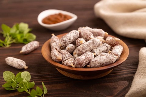 Small smoked Chicken sausages in wooden bowl on brown wooden background and linen textile. side