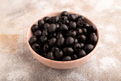 Fresh black olives in ceramic bowl on brown concrete background. side view, close up